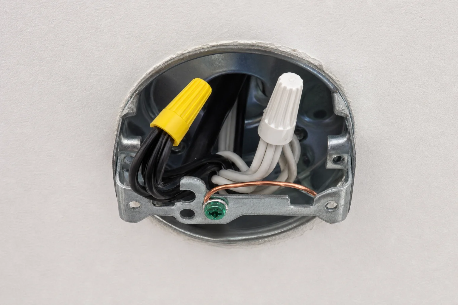 A licensed Kansas City electrician connecting black, white, and green ground wire connections inside a ceiling fan junction box, with wire nuts securing each conductor